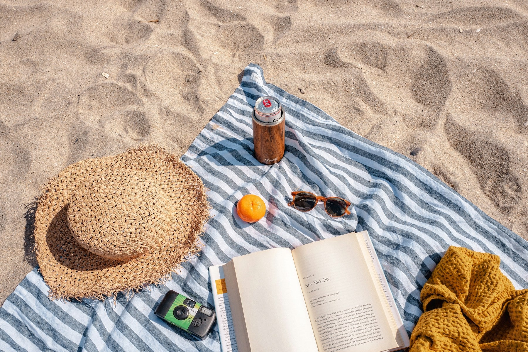 Towel with book, hat, sunglasses, camera, and drink on the beach