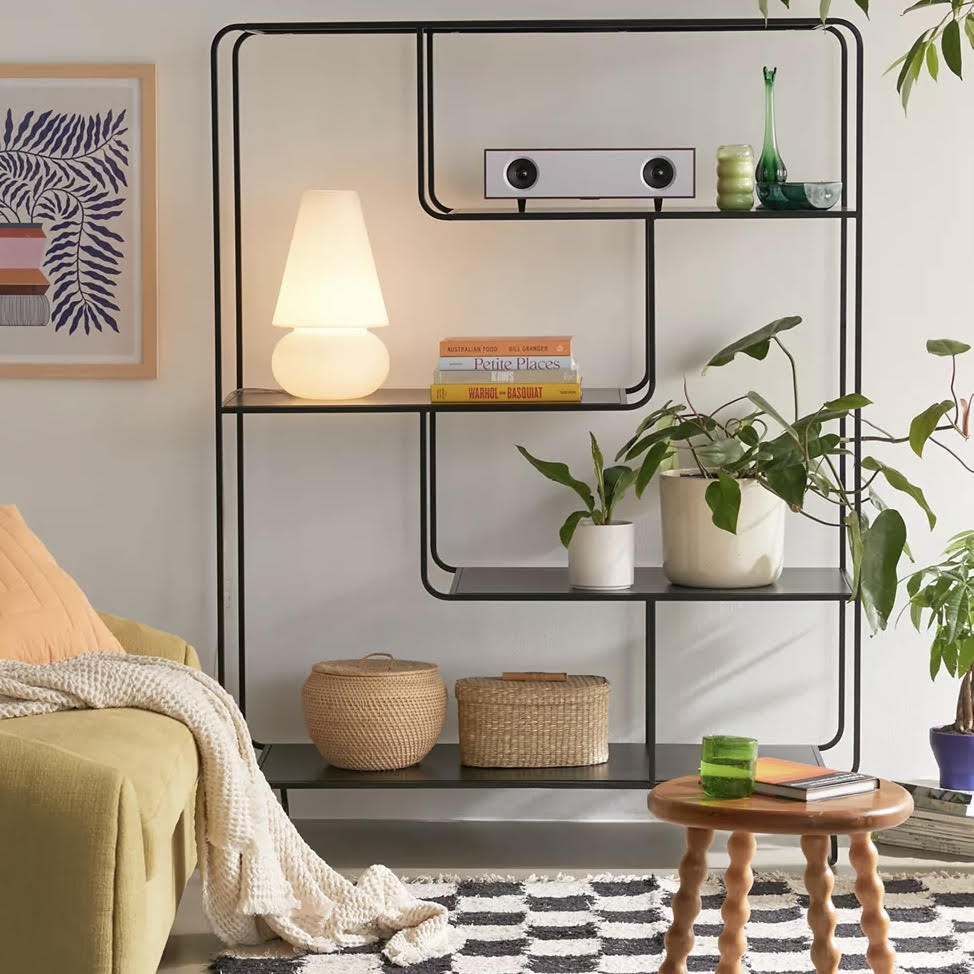 Modern living room with a black metal shelf, books, plants, and a lamp.
