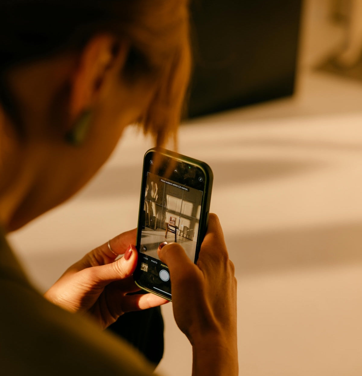 Woman taking a photo of furniture with a smartphone in a warm-toned setting