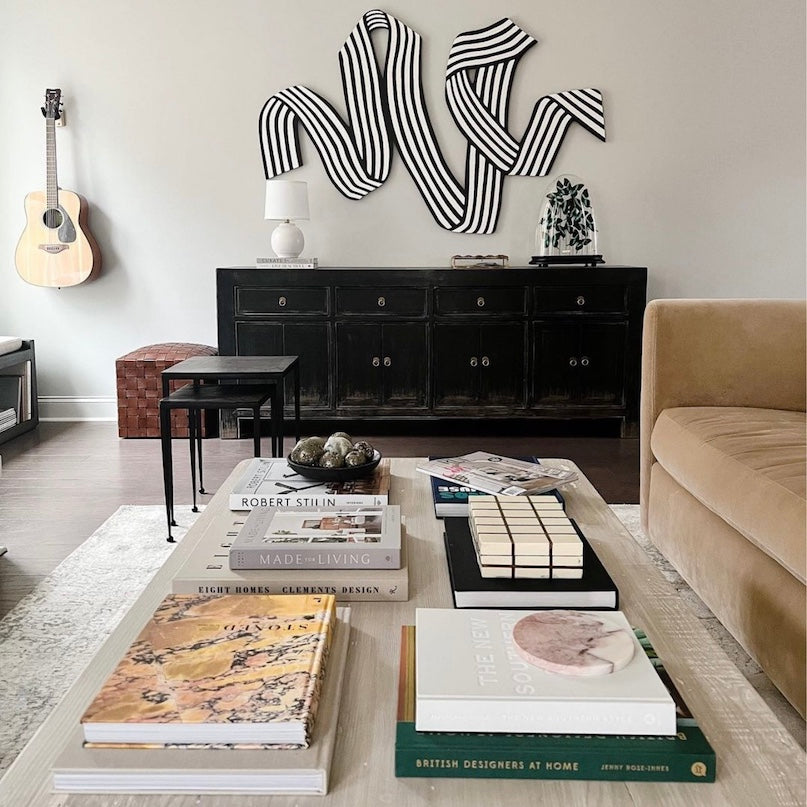 Living room with a coffee table displaying books, a guitar on the wall, and a decorative wall piece.
