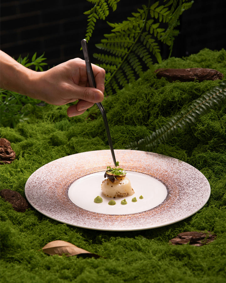 Hand plating a fine dining plate on a bed of grass