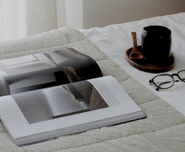 Open coffee table book on bed with a coffee mug beside it