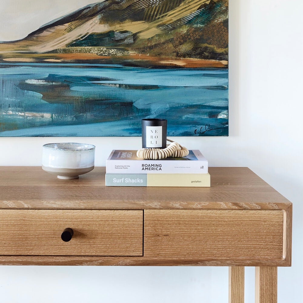 Wooden console table with decorative books against a wall with abstract art.
